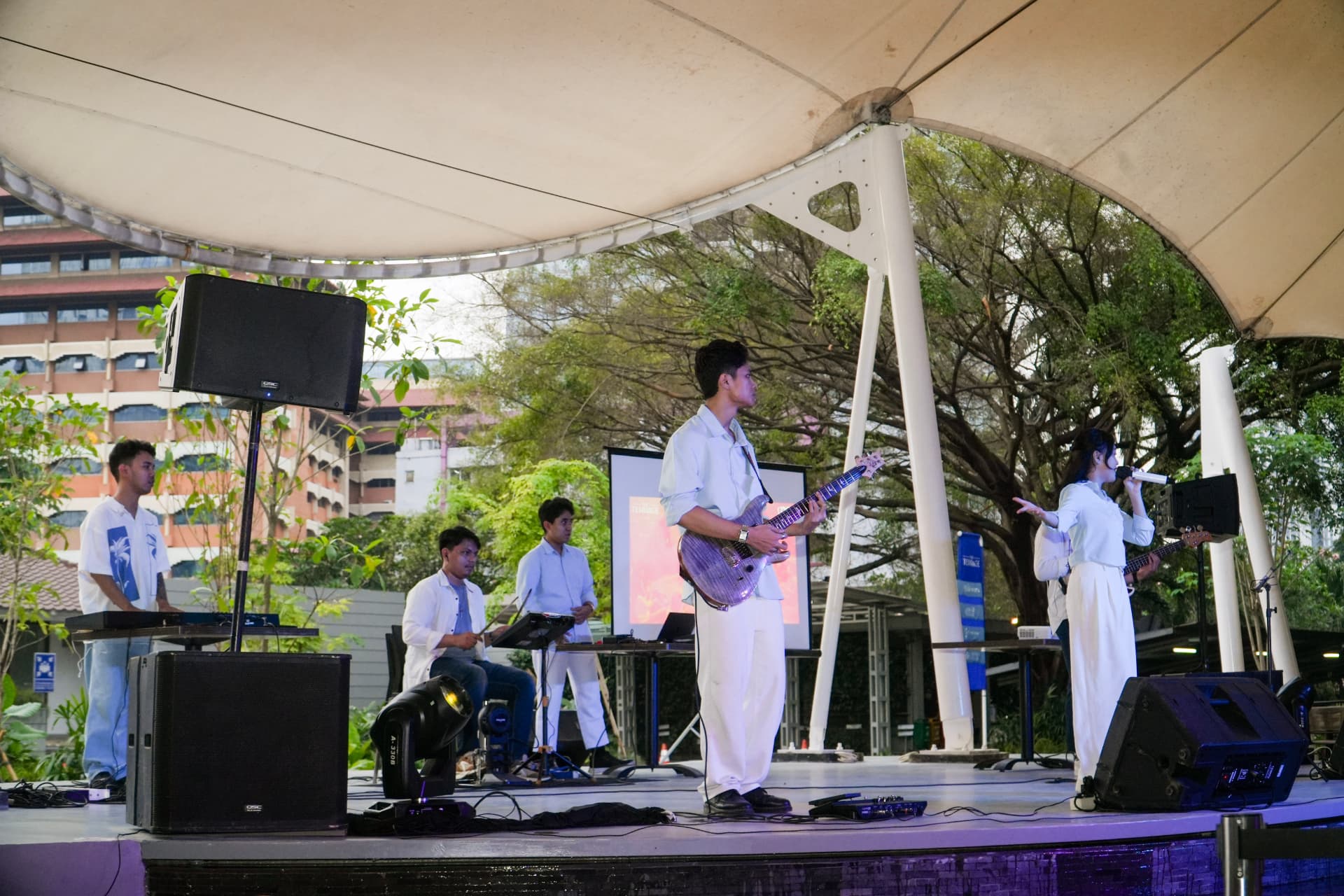 Full band in white outfits performing on an open-air stage